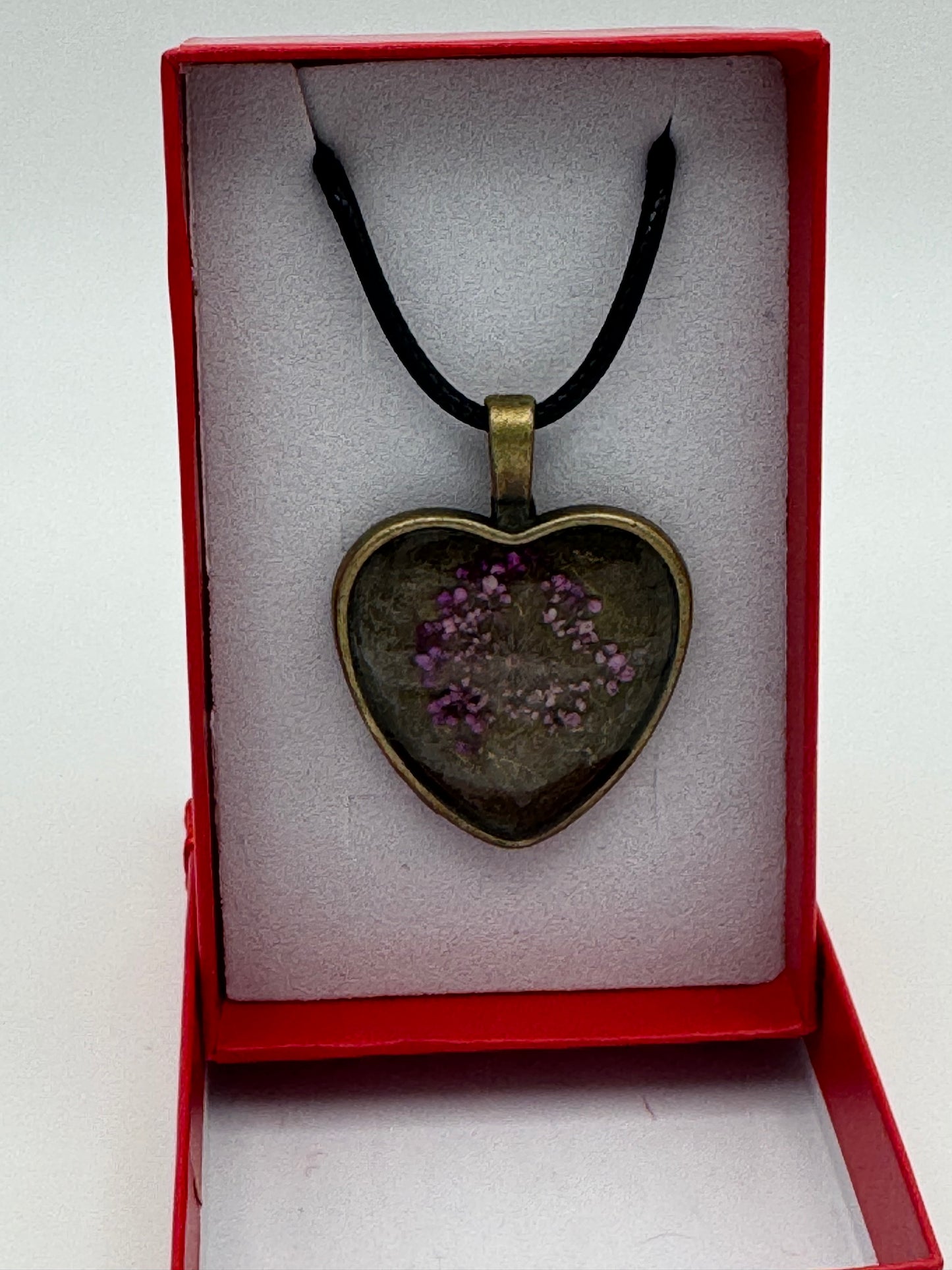 Pink flower contained in clear resin and metal bezel necklace, with black waxed chain