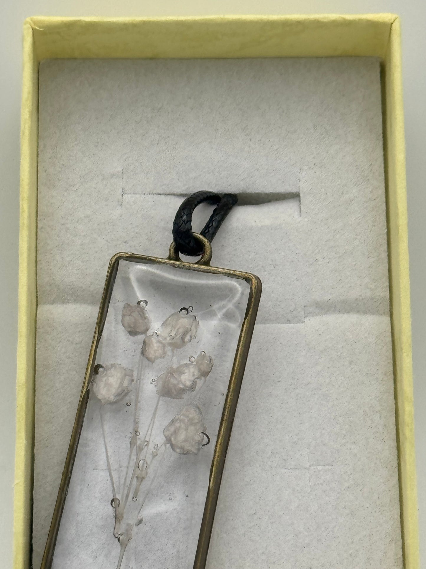 Necklace with flower encased in clear resin, on a black waxed chain