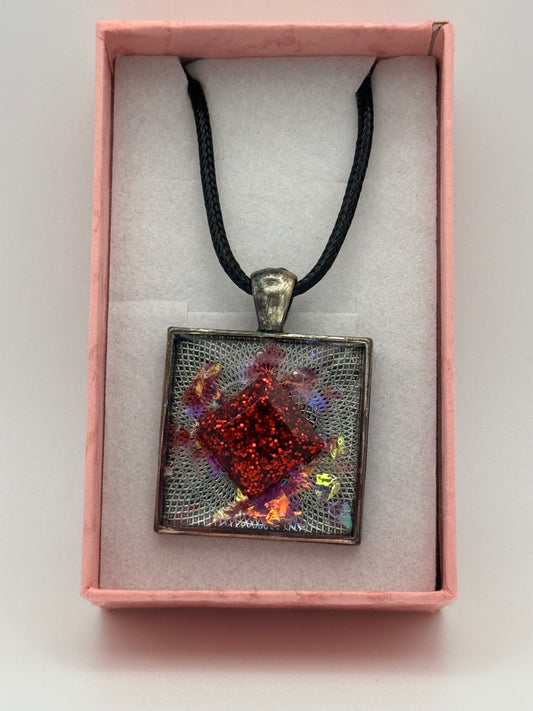 Necklace with a red diamond shape encased in clear resin, set in a metal bezel, with black waxed chain
