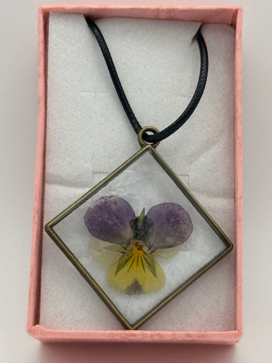 Necklace with flower encased in clear resin, on a black waxed chain