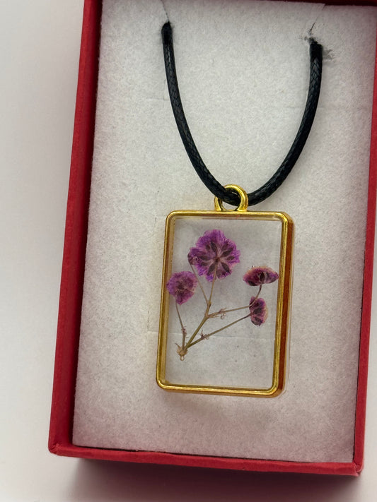 Necklace with flower encased in clear resin, on a black waxed chain