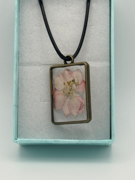 Necklace with flower encased in clear resin, on a black waxed chain