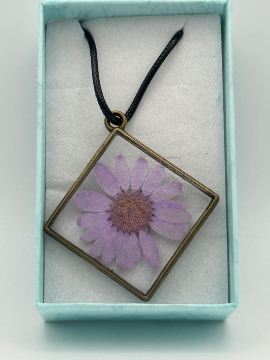 Flower encased in clear resin with a metal bezel necklace on a black waxed chain