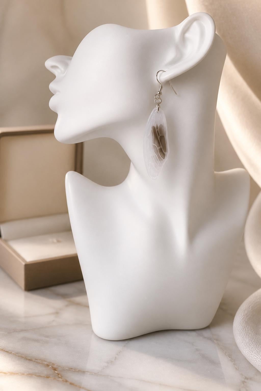 Feather-shaped earring on a white mannequin ear with a blurred background